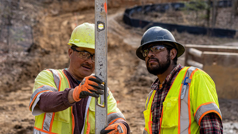 Two construction workers wearing safety vests and helmets holding a level on site